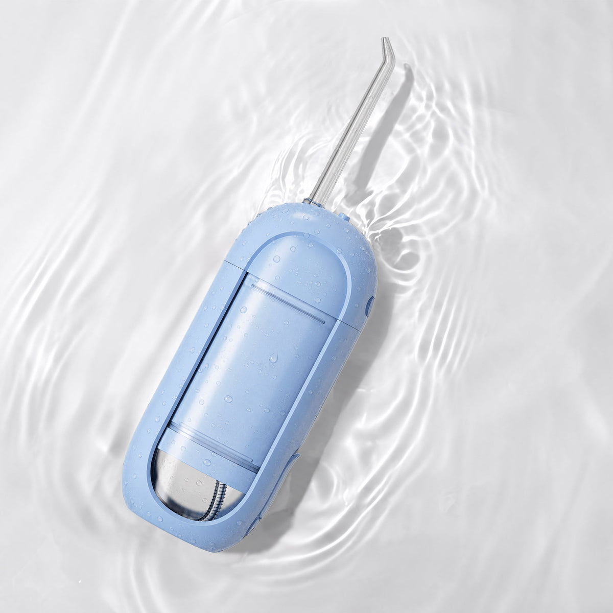 A light blue flossing device with a silver metal flossing arm, resting on ripples of water on a white background.