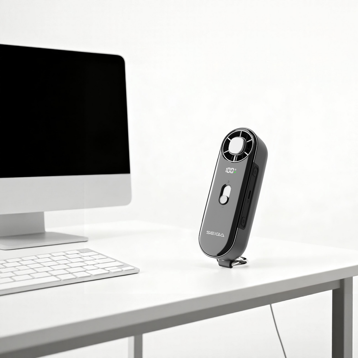 A black handheld airflow meter with a circular fan blade at the top stands on a white desk next to a computer monitor and keyboard.
