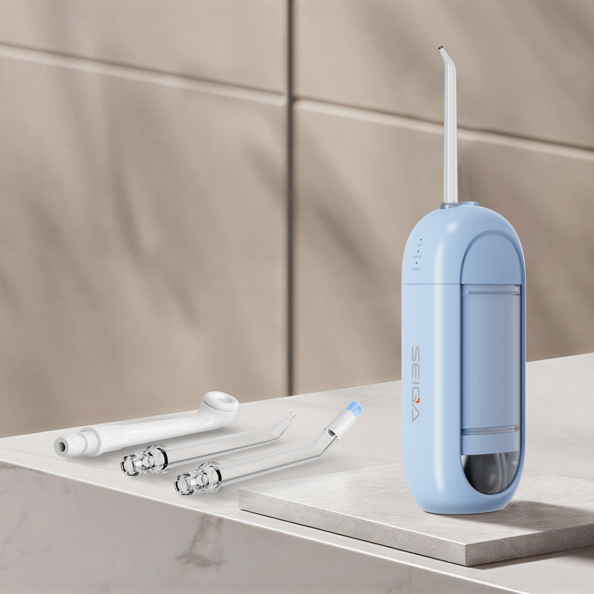 A light blue oral irrigator with a white nozzle stands on a marble-like surface, with three white replacement tips beside it against a beige tiled background.