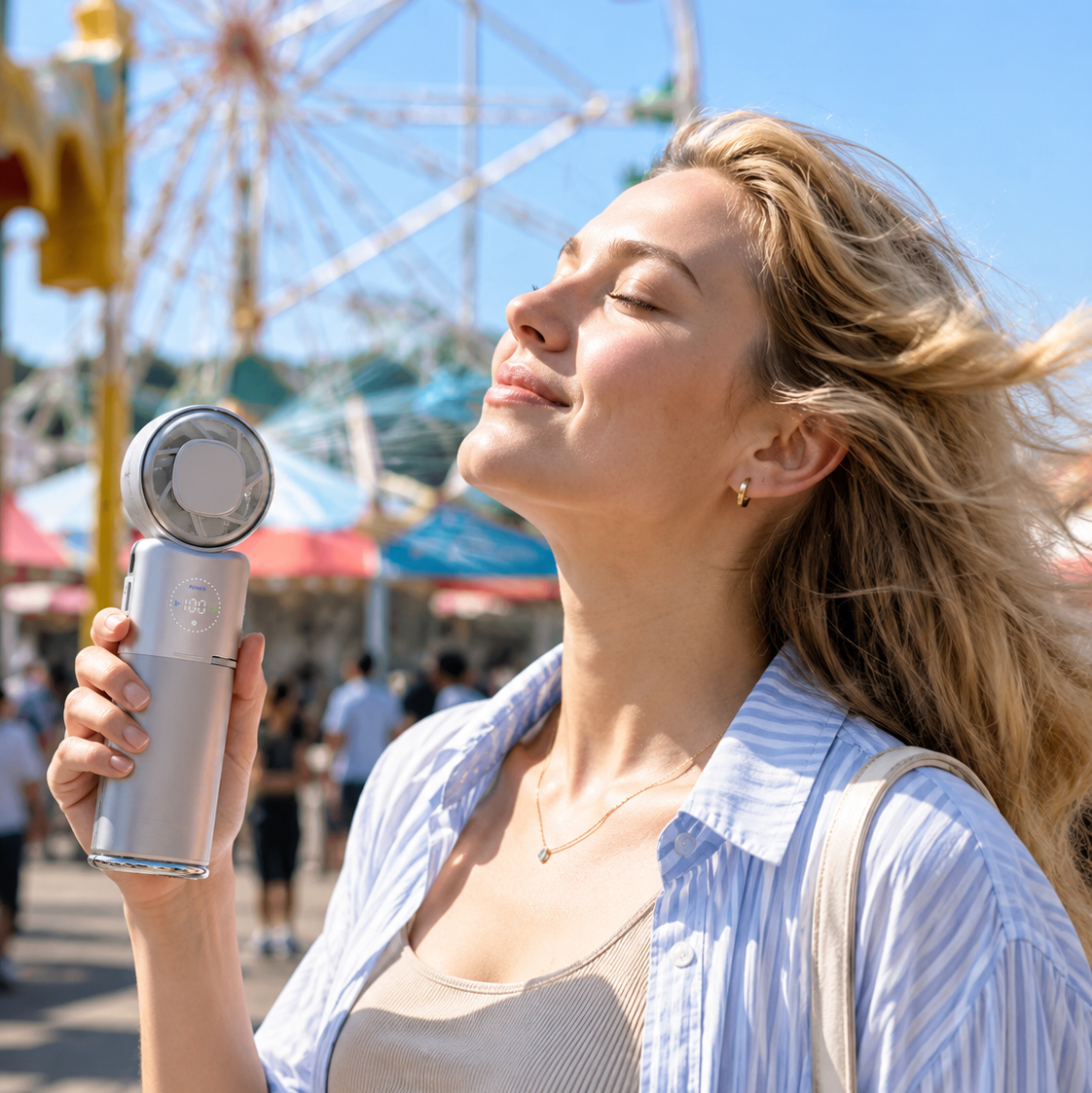A woman outdoors at a fair holding a silver handheld fan, wearing a light blue and white striped button-up shirt over a beige top, with a ferris wheel and blue sky in the background.
